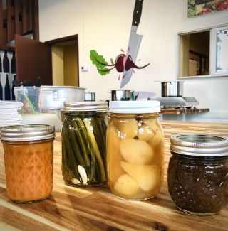 An array of purees, jams, and preserved jarred foods rest on a wooden butcher's block table at Kitchen Culture.